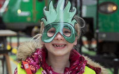 Ein Mädchen mit einer grünen Pappmaske auf dem Gesicht lacht in die Kamera