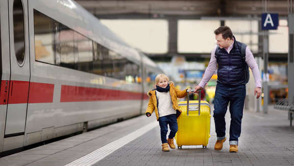 A man and a young boy with a suitcase on the platform next to a train