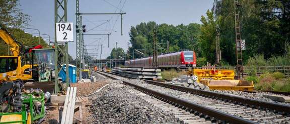 Neues Bahngleis, links Baustellenfahrzeuge, rechts S-Bahn auf bestehendem Gleis