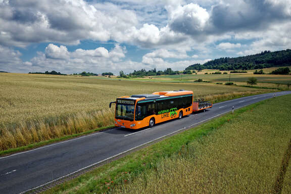 Ein orangefarbener Bus mit Fahrradanhänger fährt übers Land