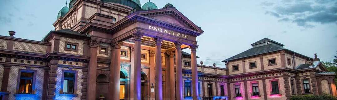 Frontansicht Kaiser-Wilhelms-Bad bei Nacht, farbig beleuchtet