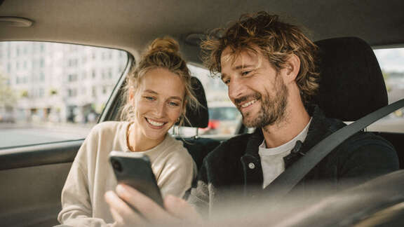 Mann und Frau sitzen in einem Auto und schauen auf ein Smartphone.
