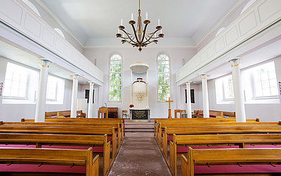 Vergrößerte Ansicht: Innenansicht der Kirche, braune Sitzbänke und helle Wände