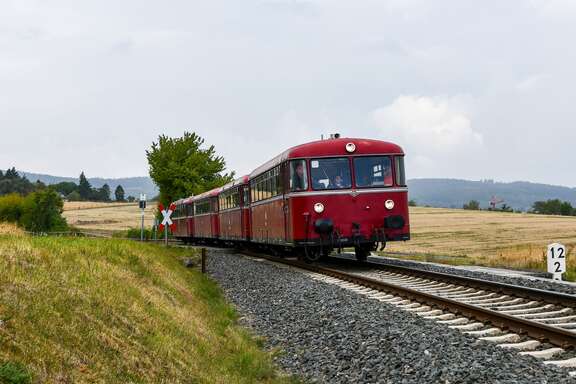 Schienenbus-Sonderfahrt durch den Odenwald Ein roter Zug fährt auf Schienen durch eine idyllische und sonnige Landschaft