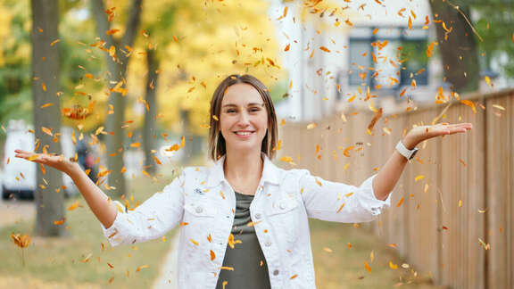 Young woman smiling and throwing autumn leaves in the air