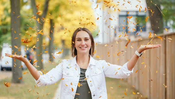 lachende Frau mit erhobenen Händen wirft gelbe Blätter in die Luft