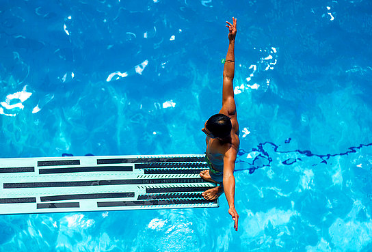 Mann steht auf einem Sprungturm im Freibad