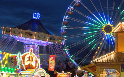Kettenkarussell, Riesenrad und Jahrmarktbuden beleuchtet am Abend