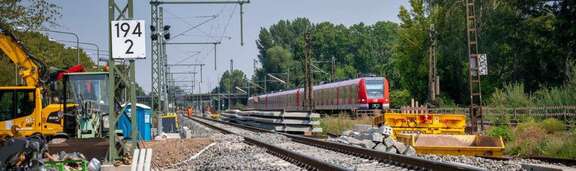 Neues Bahngleis, links Baustellenfahrzeuge, rechts S-Bahn auf bestehendem Gleis