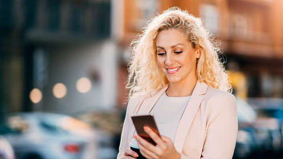 Smiling blond woman on the street looking on her mobile phone