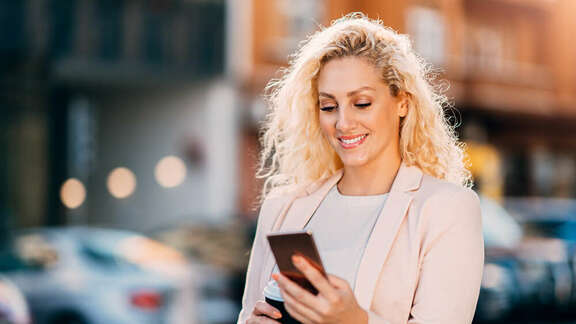 Smiling blond woman on the street looking on her mobile phone