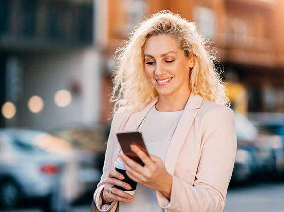 Smiling blond woman on the street looking on her mobile phone