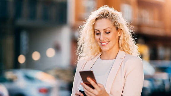 Smiling blond woman on the street looking on her mobile phone