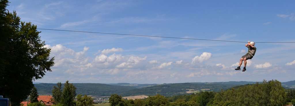 Europa-Seilbahn im Kletterwald Steinau Ein Mann rutscht an einem senkrechten Seil über Baumwipfel hinweg