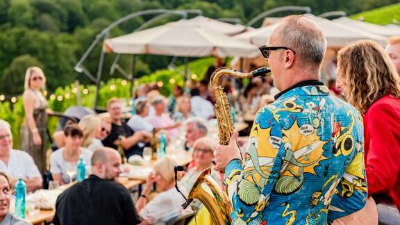 Saxophonspieler vor Gästen in einem Weinberg.