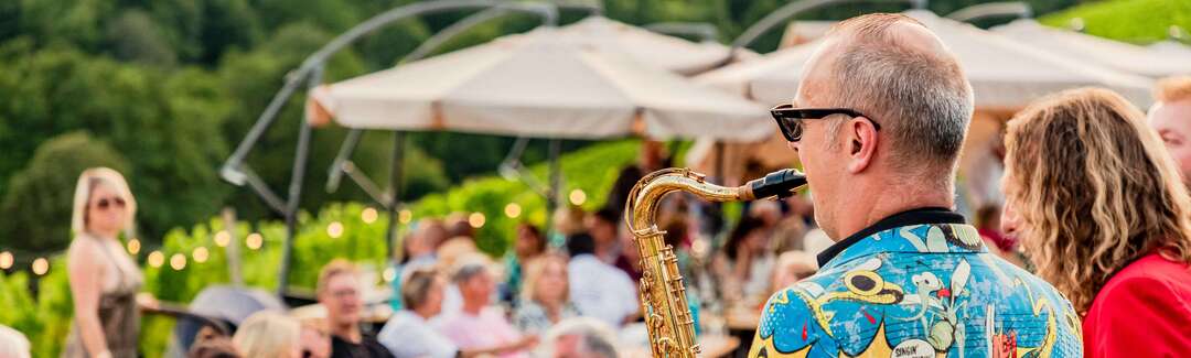 Saxophonspieler vor Gästen in einem Weinberg.