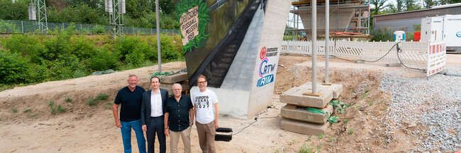Vor dem Brückenpfeiler (v.l.n.r.): Prof. Knut Ringat (RMV), Julien Zamberk (Eintracht Frankfurt), Horst Amann (RTW Planungsgesellschaft) und der Frankfurter Mobilitätsdezernent Wolfgang Siefert (v. l.) vor dem von Fan-Vertretern der Eintracht Frankfurt gestalteten Mural am Frankfurter Waldstadion.