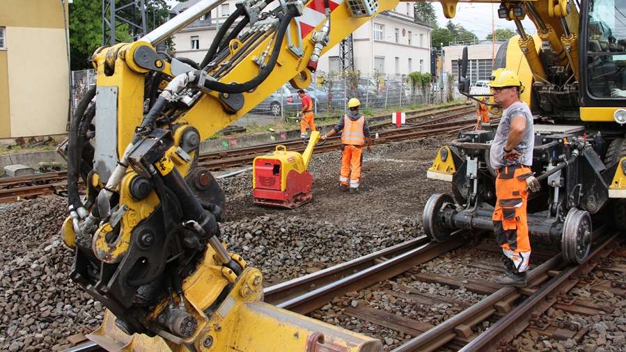 Bagger auf Gleis mit Bauarbeitern