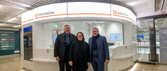 Drei Personen stehen vor einer Information der Deutschen Bahn.