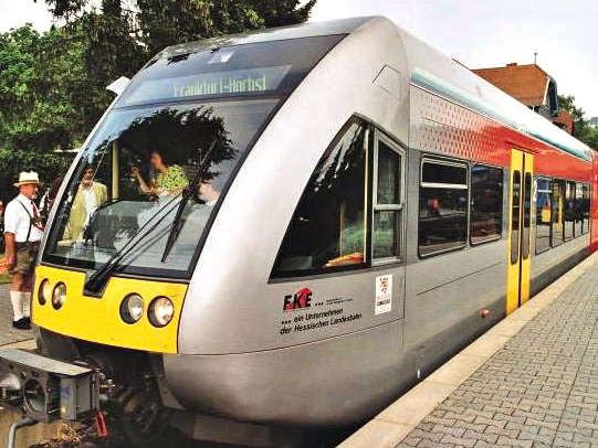 Vergrößerte Ansicht: Grauer Zug mit gelben und roten Elementen steht am Bahnhof