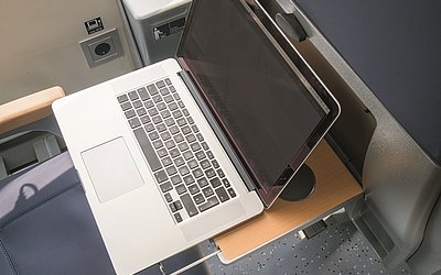 Vergrößerte Ansicht: Die Ablagefläche an jedem Sitz bietet genug Platz für einen Laptop, eine Steckdose versorgt Fahrgäste mit Strom