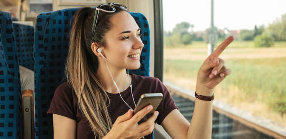 Junge Frau in der Bahn mit Handy und Kopfhörern deutet auf Fenster