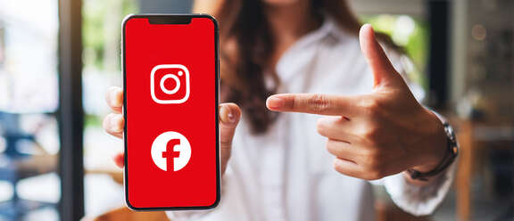 Frau zeigt auf ein Smartphone mit rotem Bildschirm, auf dem die Symbole von Instagram und Facebook zu sehen sind.