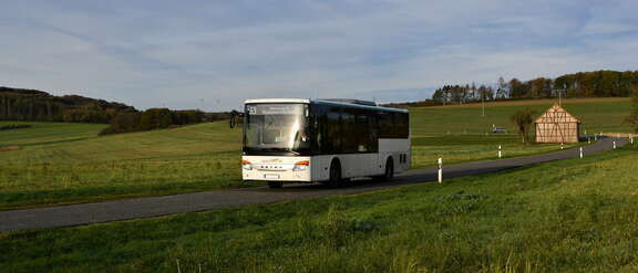 Ein Bus fährt in einer leicht hügeligen Landschaft inmitten grüner Wiesen.