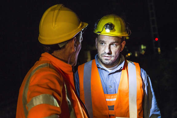 Gespräch von Bauarbeitern bei Helmlicht Zwei Männer in Arbeitskleidung unterhalten sich im Tunnel