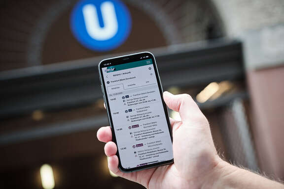 RMV-Auslastungsprognose Ein Handy vor einem U-Bahn-Stationseingang, auf dem Display wird eine Verbindung mit Auslastungsprognose angezeigt.