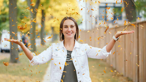 Young woman smiling and throwing autumn leaves in the air