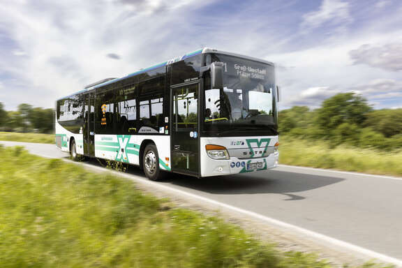 Bus mit Aufschrift X auf Straße in grüner Landschaft