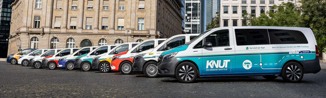 Autos stehen seitlich in einer Reihe leicht versetzt auf einem Platz vor einem historischen Gebäude. Im Hintergrund Hochhaus