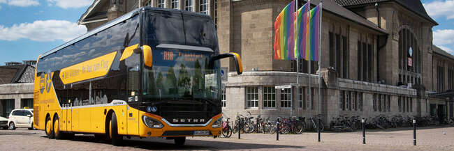 Airliner Ein orangefarbener Bus mit Aufschrift AirLiner steht vor einem Bahnhofsgebäude