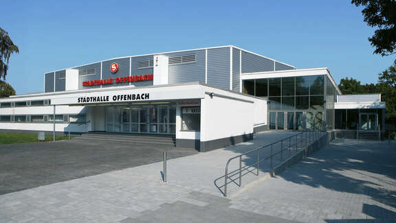 Two-story, flat white building with glass extension with the lettering "Stadthalle Offenbach"