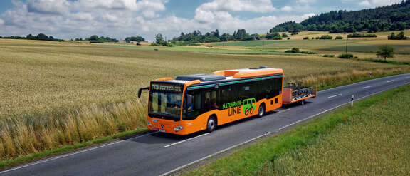 Ein orangefarbener Bus mit Fahrradanhänger fährt übers Land