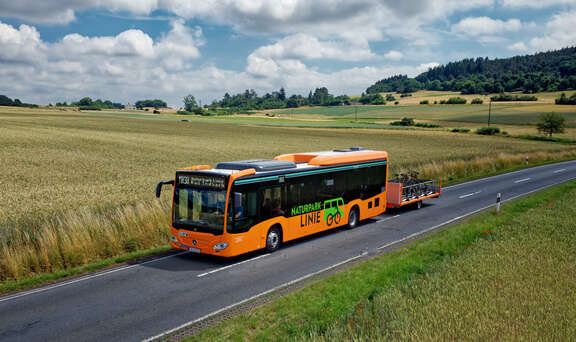 Ein orangefarbener Bus mit Fahrradanhänger fährt übers Land