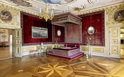 Innenansicht des kurfürstlichen Gemachs mit Parkettboden, Stuckdecken und weinrotem Himmelbett. undgoldverzierten Wänden.