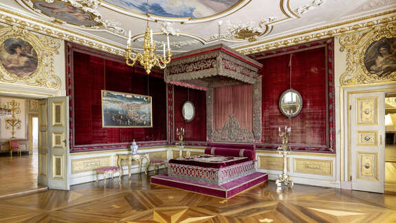 Innenansicht des kurfürstlichen Gemachs mit Parkettboden, Stuckdecken und weinrotem Himmelbett. undgoldverzierten Wänden.