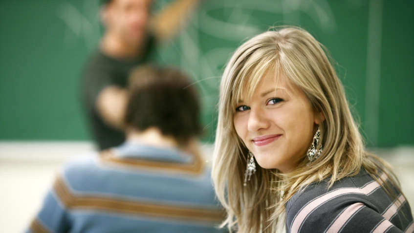Schülerin im Klassenzimmer vor Tafel schaut hinter sich