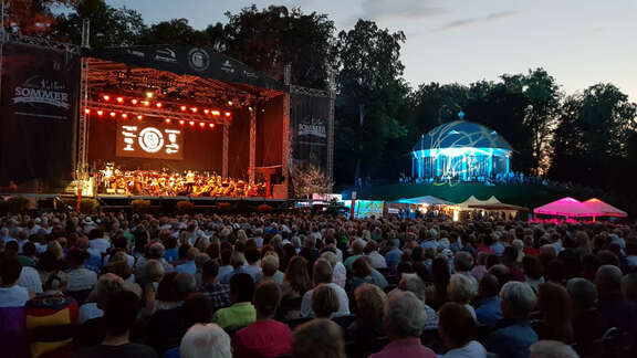 Open-Air-Bühne vor Bäumen und Publikum in der Abenddämmerung