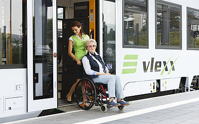 Vergrößerte Ansicht: Zugbegleiterin schiebt Seniorin im Rollstuhl über die Rampe aus dem Zug