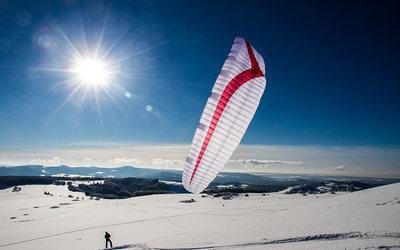 Ein weißer Fallschirm mit einem roten Streifen steht auf Schneeboden, die Sonne scheint 