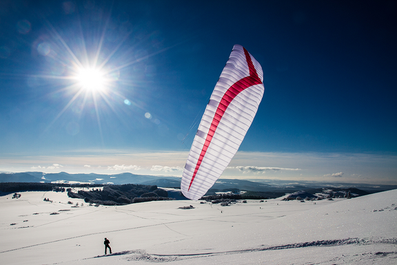 Ein weißer Fallschirm mit einem roten Streifen steht auf Schneeboden, die Sonne scheint 