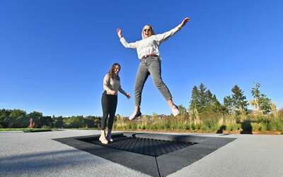 Zwei Frauen hüpfen auf einem ebenerdigen Trampolin unter freiem Himmel