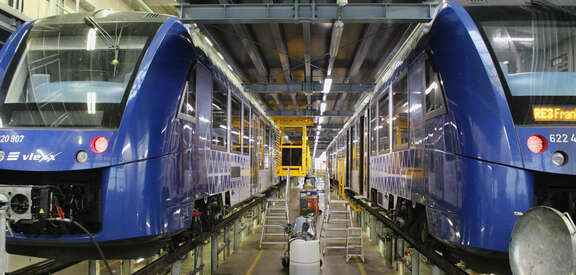 Zwei blaue Züge stehen auf Hochgleisen in einer großen Halle