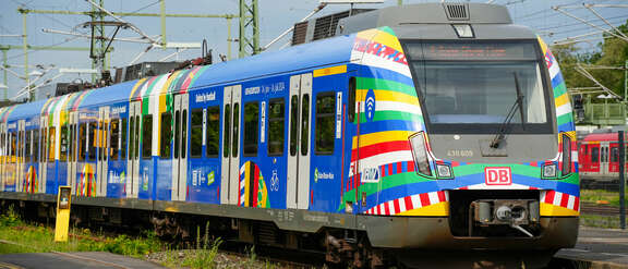 Eine bunt beklebte S-Bahn im EM-Design mit vielen verschiedenen Farben fährt durch Frankfurt.
