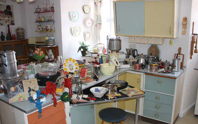 Blick in Küche: Küchenschrank, Arbeitsfläche in hellen Farben, im Hintergrund Sitzecke