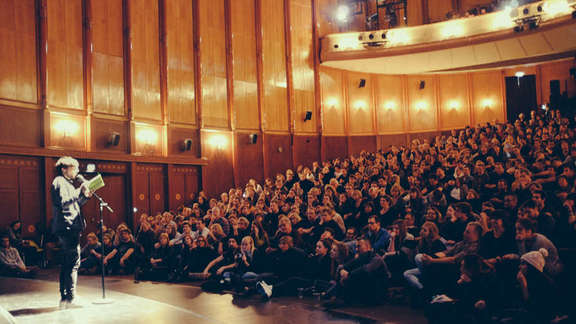Visitors in a large hall look at man on stage