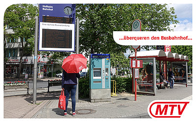 Eine Frau mit rotem MTV-Regenschirm steht vor der Fahrplanauskunft eines Busbahnhofs: ...überqueren den Busbahnhof... 